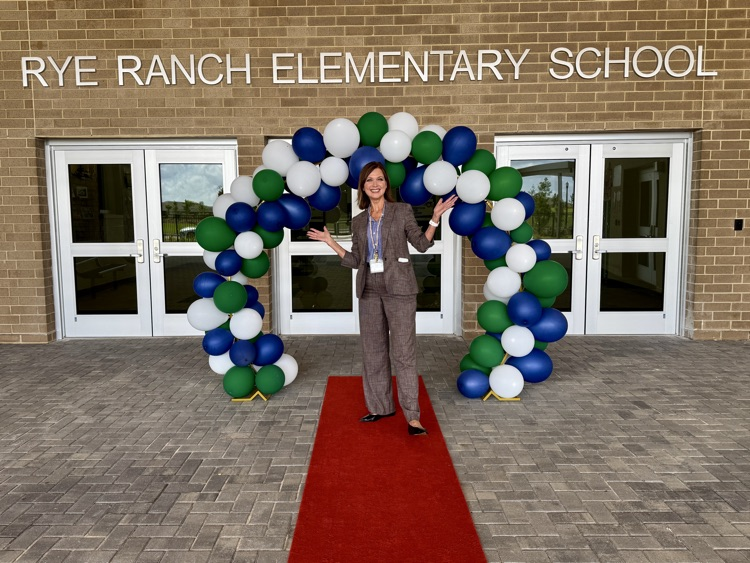 A principal standing on a red carpet with a balloon archway behind her