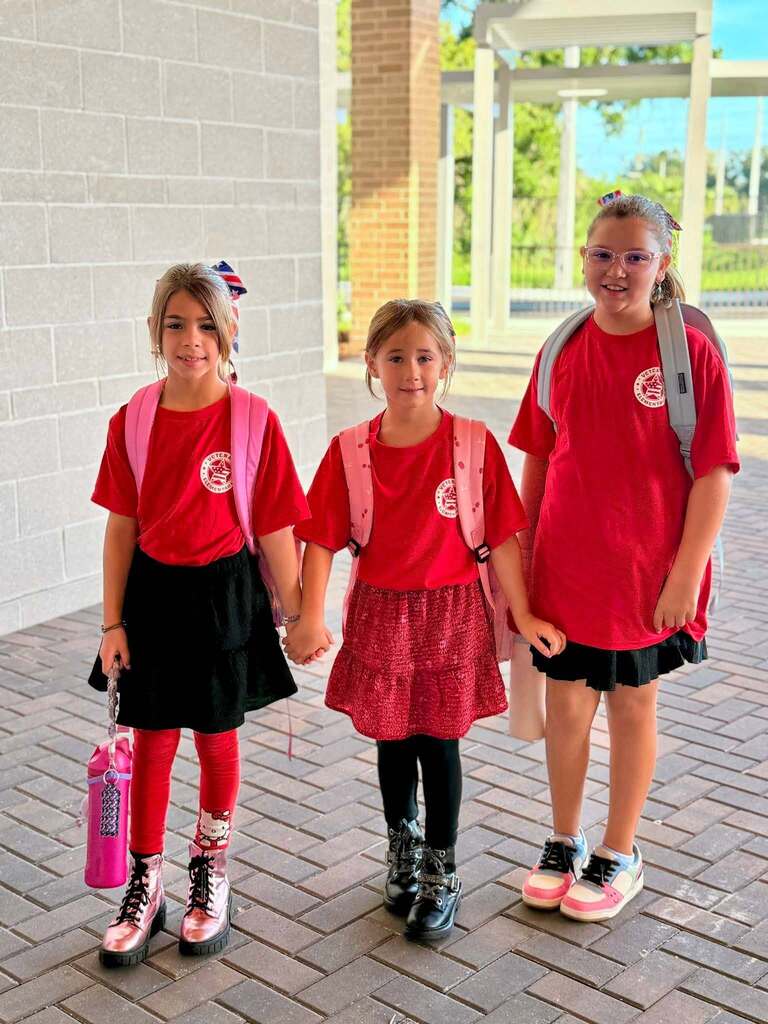 Three girls holding hands and wearing red shirts on the first day of school.
