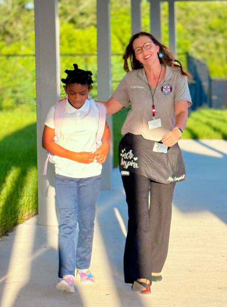 A school principal smiling as she walks down a walkway with a student.