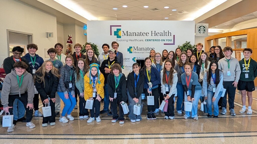 Students gathered in front of a hospital sign reading 'Manatee Health'.
