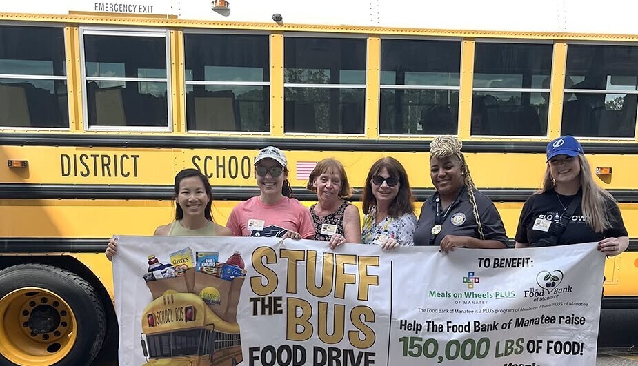 Volunteers hold a banner in front of a school bus promoting a food drive