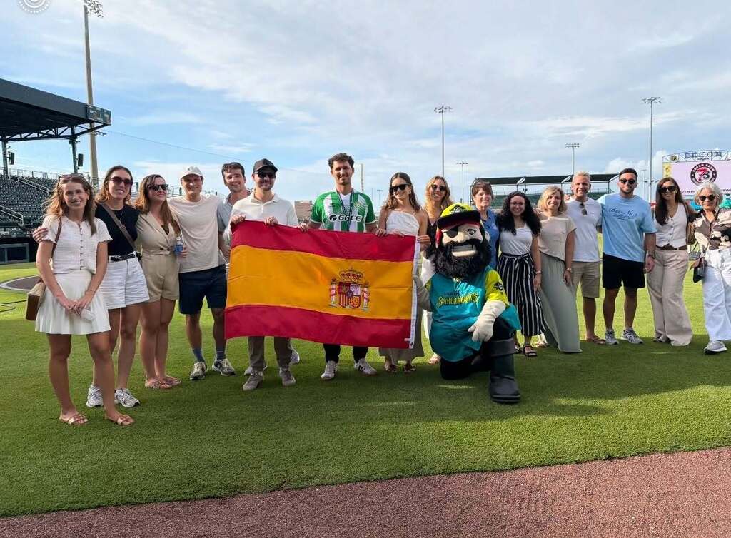 Men and women lined up on a baseball field while holding a flag from Spain.