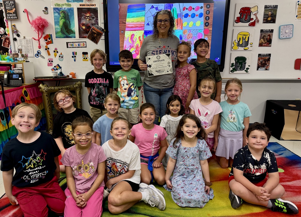 A teacher standing in a classroom with students surrounding her.