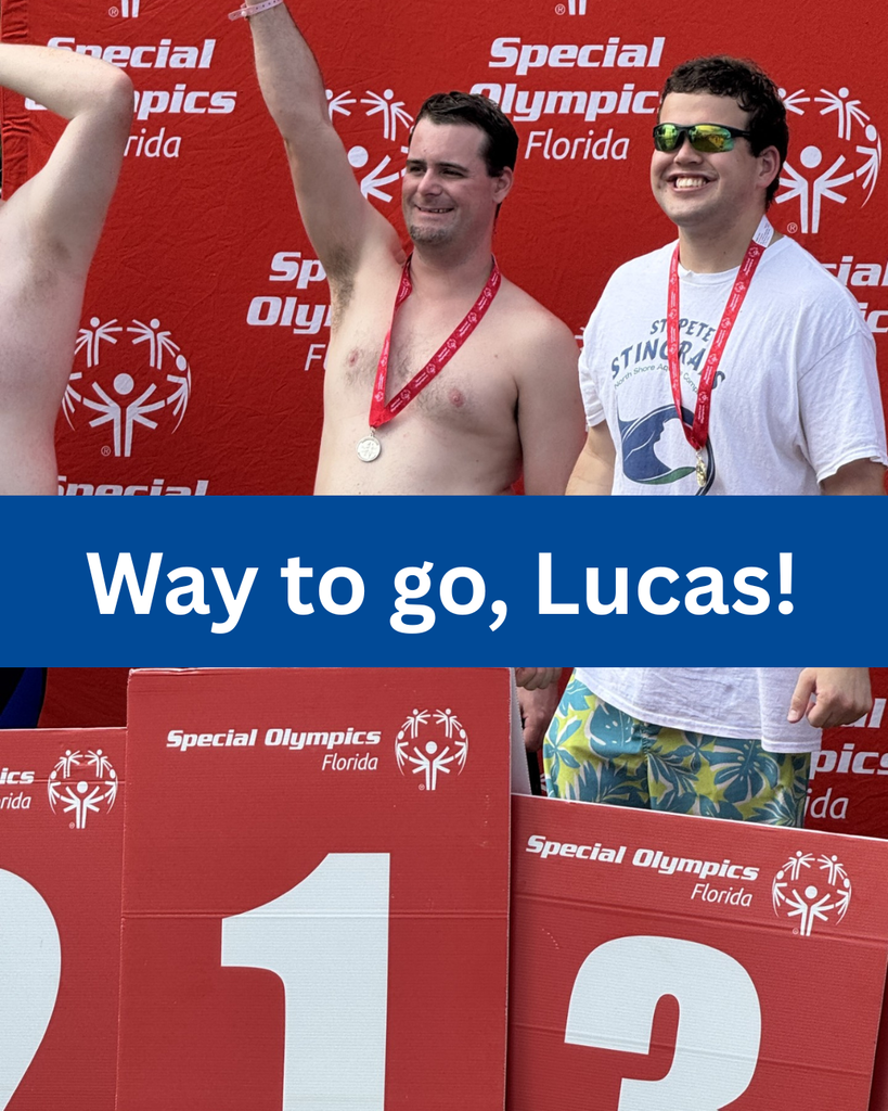 A swimmer stands on the first place podium holding up his arm in celebration.
