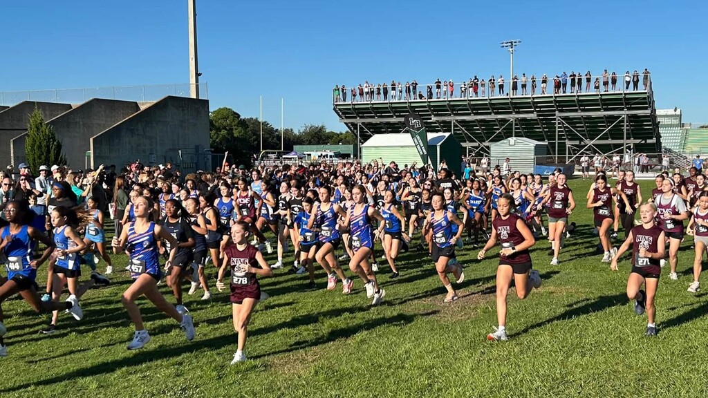Middle school runners at a cross country meet as parents line the top of the bleachers looking on