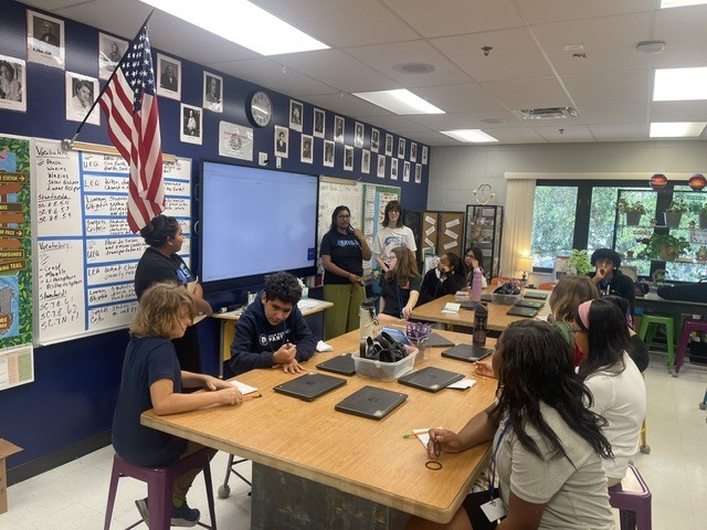 Students sitting at desks while listening to volunteer educators speaking in their classroom