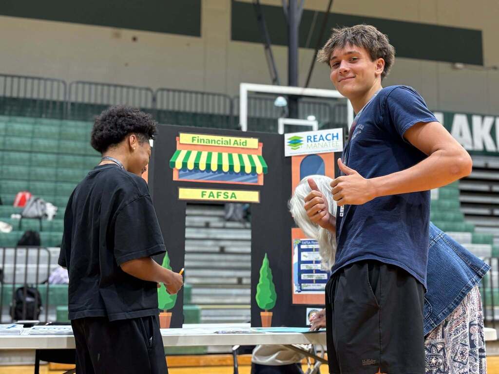 A boy in a blue tshirt and black shorts giving two thumbs up in a high school gym