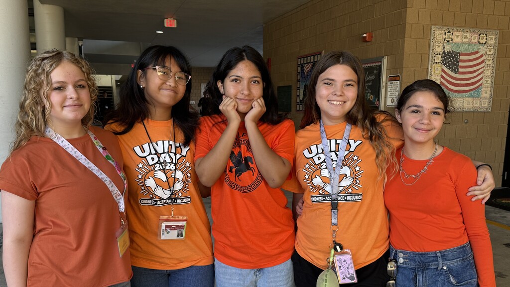 Students standing shoulder to shoulder while wearing orange shirts.