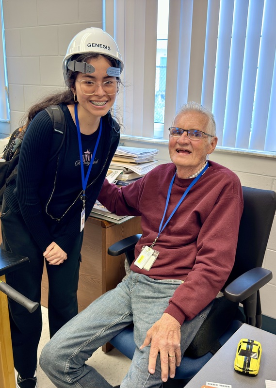 A student wearing a construction hat smiles with teacher