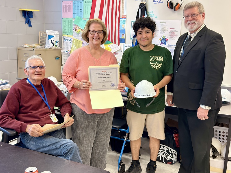 Adults smiling as a student holds a construction hat in hand.