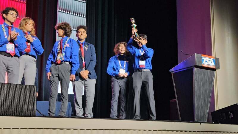 Students in blue dress shirts holding a trophy above their heads.