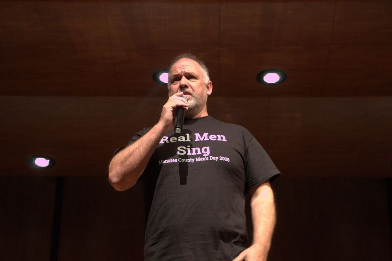 A music educator holding a microphone and speaking into it.