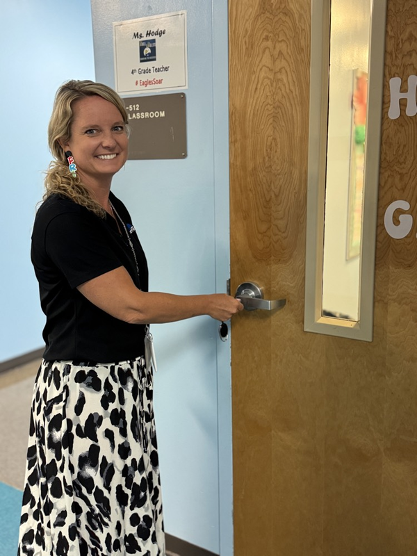 A teacher holding the door knob of a classroom and smiling