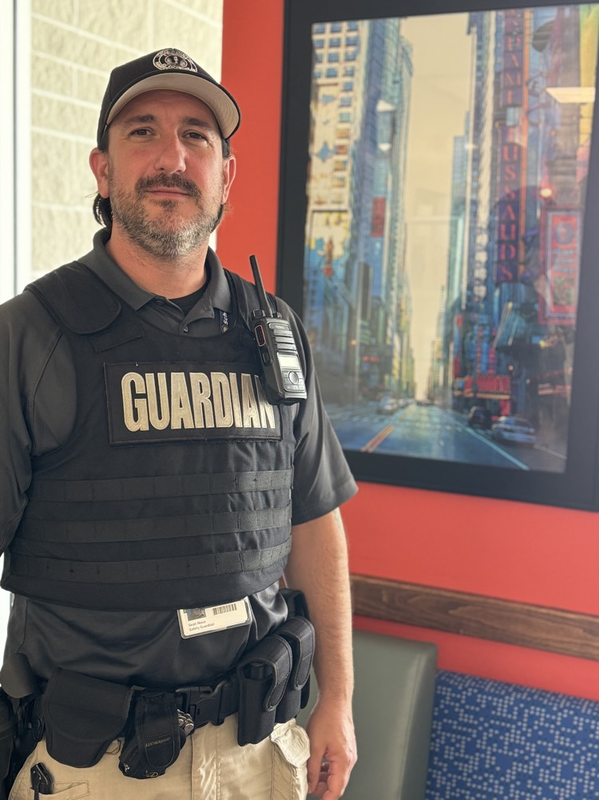 A school safety guardian stands in front of an artwork depicting Times Square in New York City