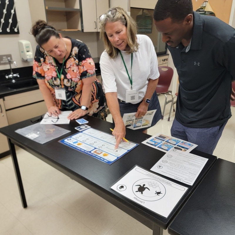 Teachers examine science lessons covering a classroom table.