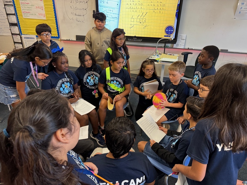 A group of students sitting around a circle collaborating to answer questions.