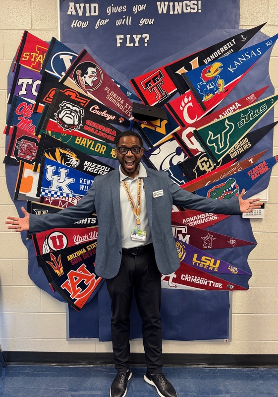 Jamara Clark stands in front of a collage of college pennants with the message: AVID gives you wings
