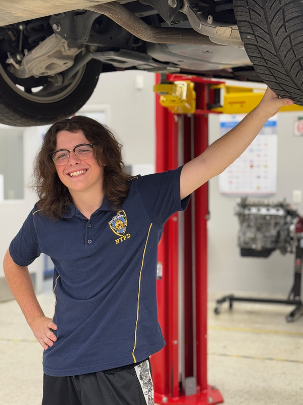 A young man stands under a vehicle inside a mechanics garage at his high school