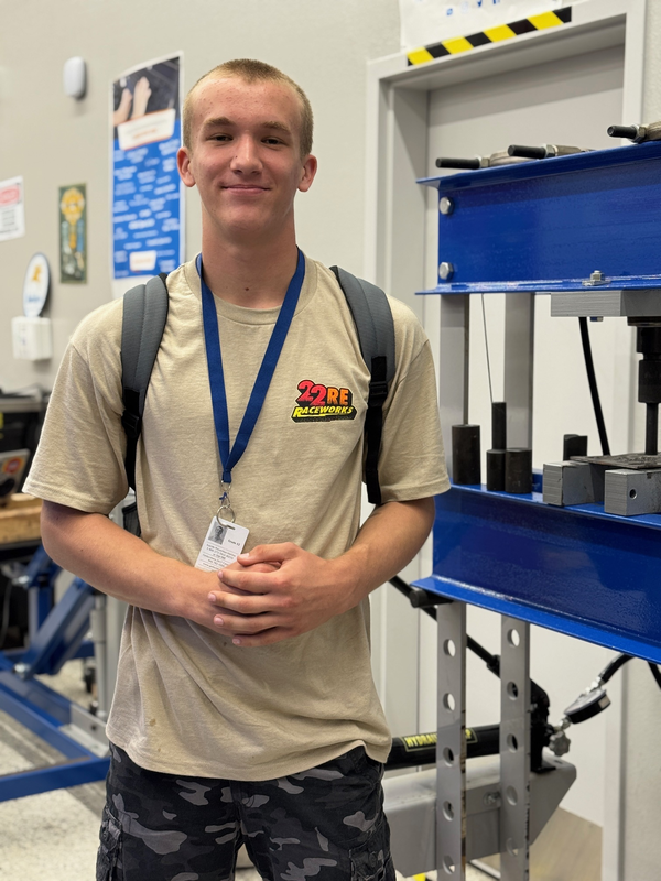 A young man smiles in an automotive garage at his high school