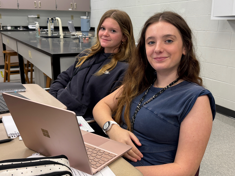Two teens smiling while working on their laptop computers.