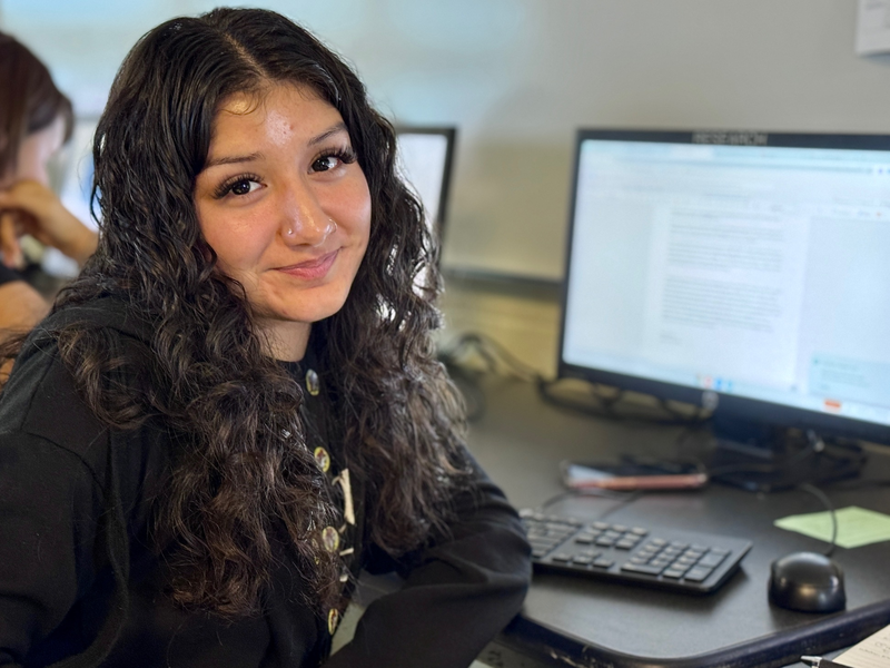 A student reporter sitting next to her computer while smiling.