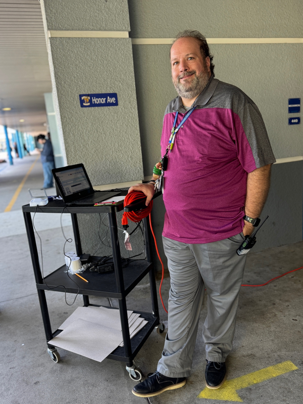 An educator standing next to a rolling shelf with a laptop computer on top.