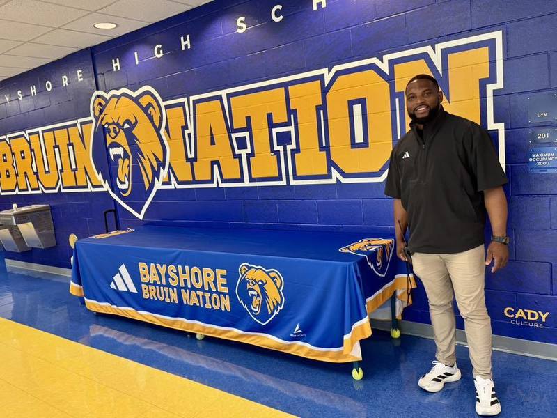 A man stands in front of a wall mural which reads, "Bruin Nation".