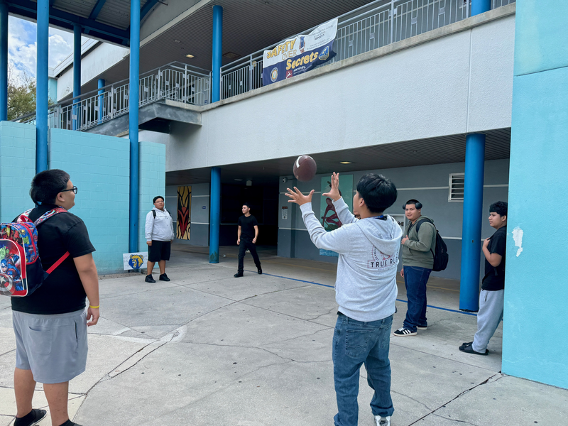 Students tossing a football in the courtyard of a high school during lunch.