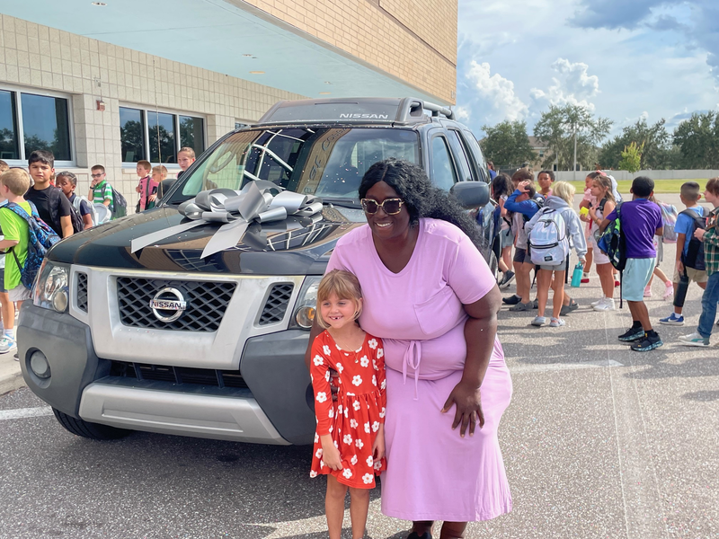 Laron, a teacher aide, smiling in front of her new vehicle with a student.