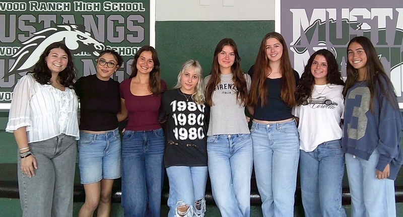 Teens standing in front of a banner featuring their mascot, the Mustangs