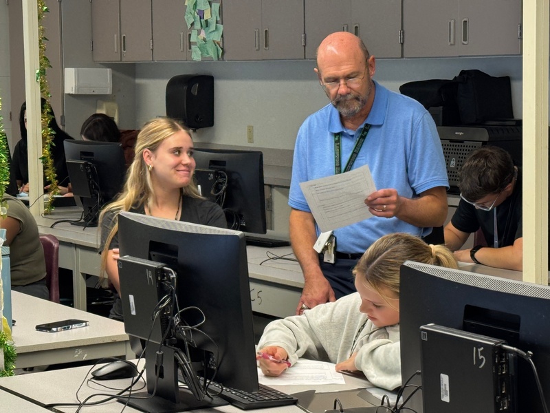 A student smiles as a teacher looks over her paper.