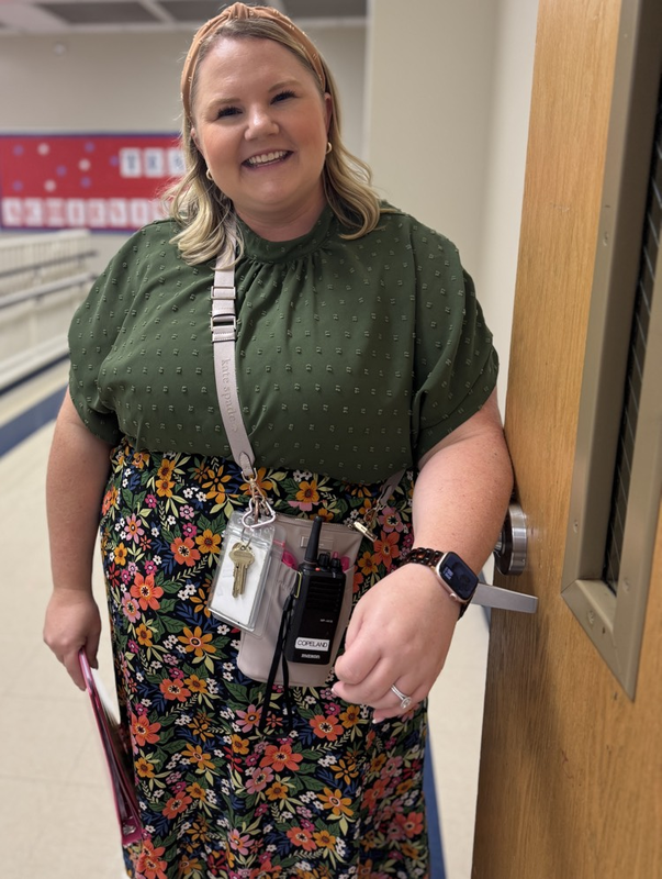 A school employee wearing a green shirt means up against the door, smiling