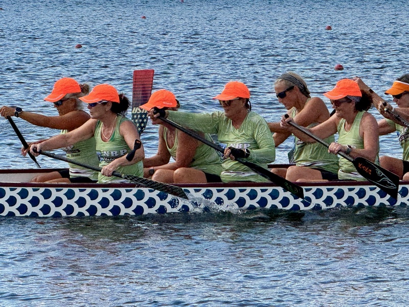 Dragon boat paddlers wearing orange hats and green shirts.