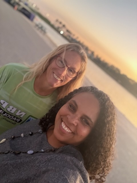 Two women smiling with the sunset behind them.