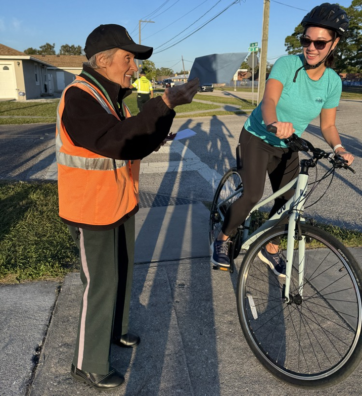A crossing guard helps a family across the street in their bicycles