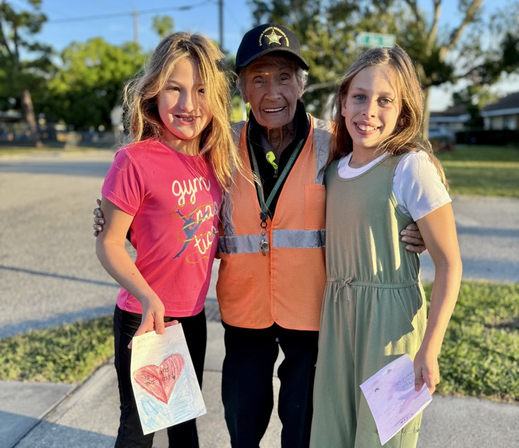 two young girls smile for a photo with their school crossing guard