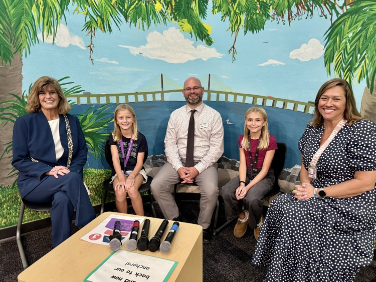 Three adults and children sitting and smiling in a school TV studio