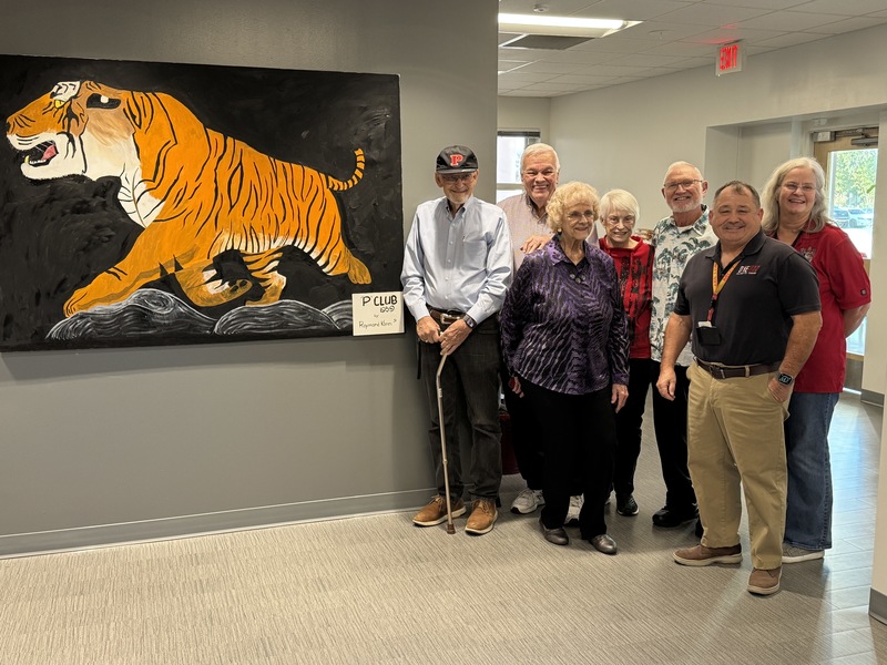 Palmetto alumni and staff stand next to a new mural hanging on the wall.