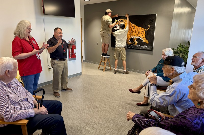 Workers install a tiger artwork while old classmates gather at Palmetto High
