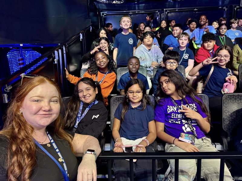 A smiling teacher with students also smiling behind her.
