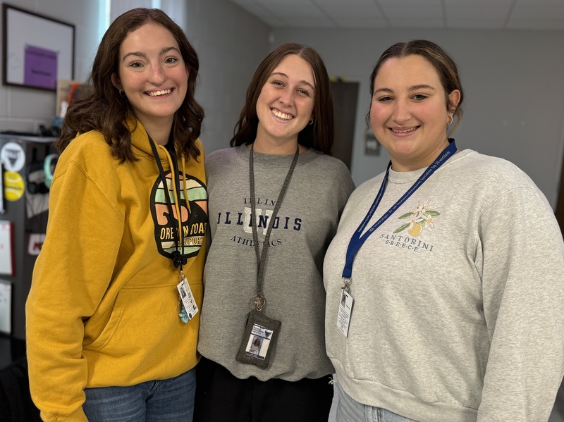 Three high school students smiling in a classroom.