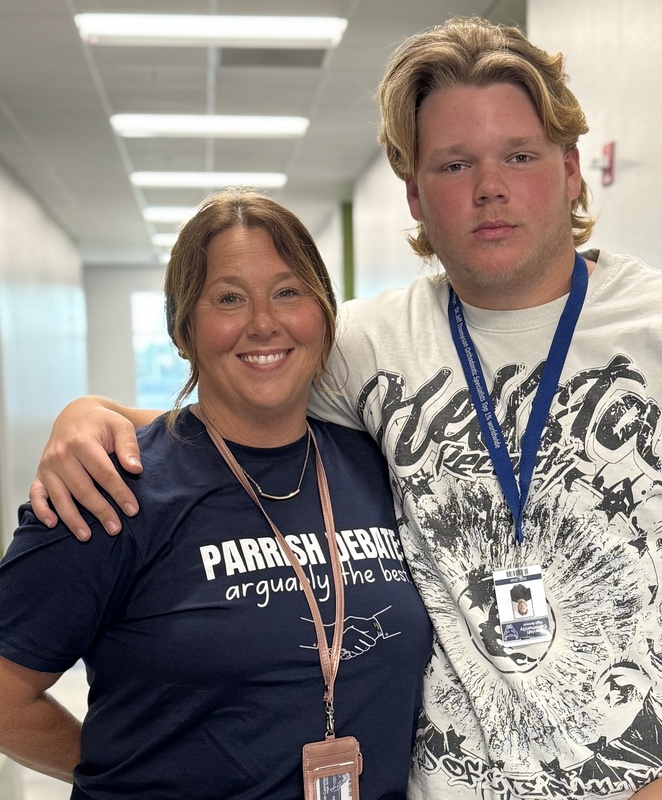 A smiling teacher and her son with his arm wrapped around her.