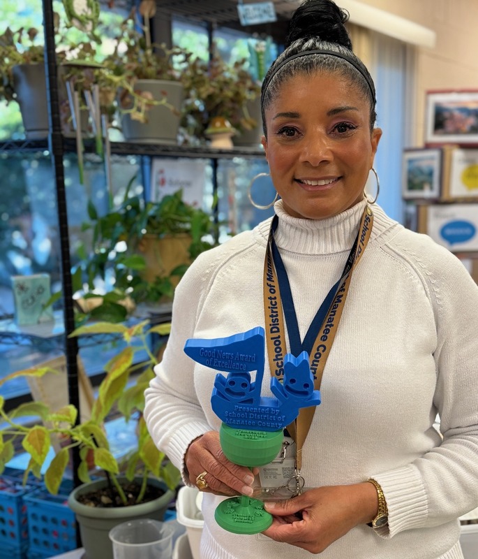 teacher holding a trophy with plants in the background.