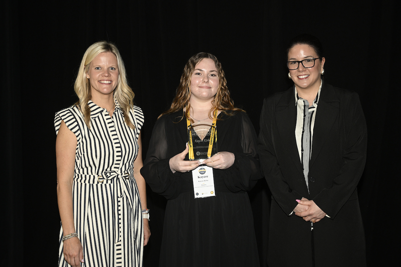 Two educators standing with a teenaged student holding a glass trophy.