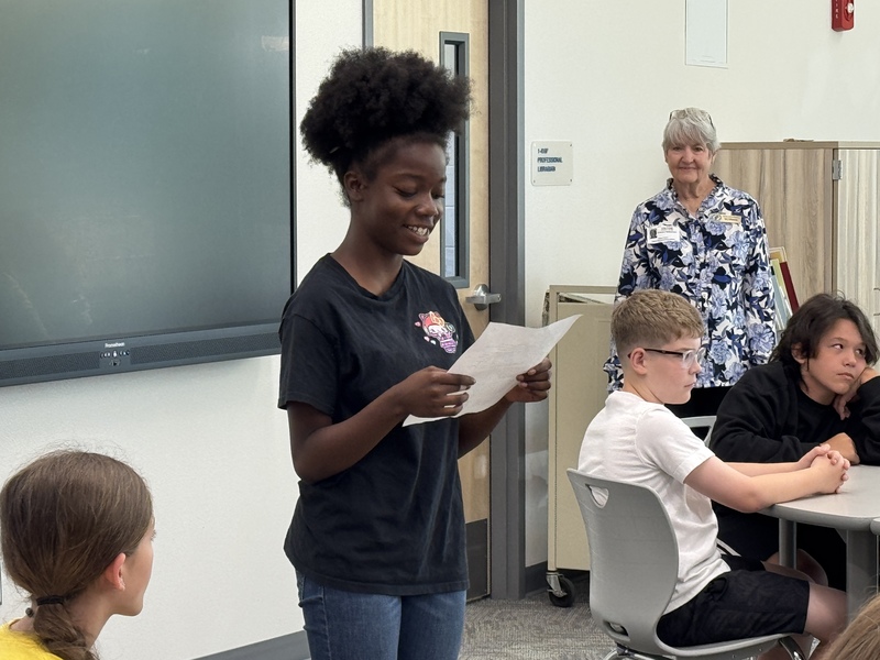 a young girl wearing a black tshirt and jeans smiles while reading her award winning essay.
