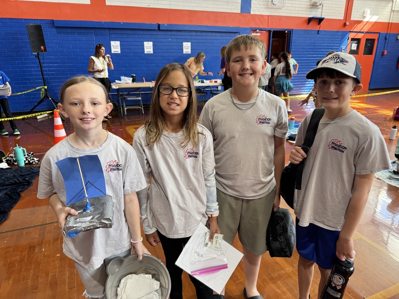 Students smiling while wearing school tshirts in a high school gymnasium.