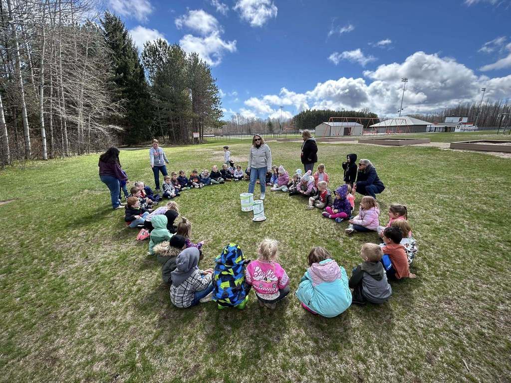 Students sit in circle outdoors while learning about butterflies