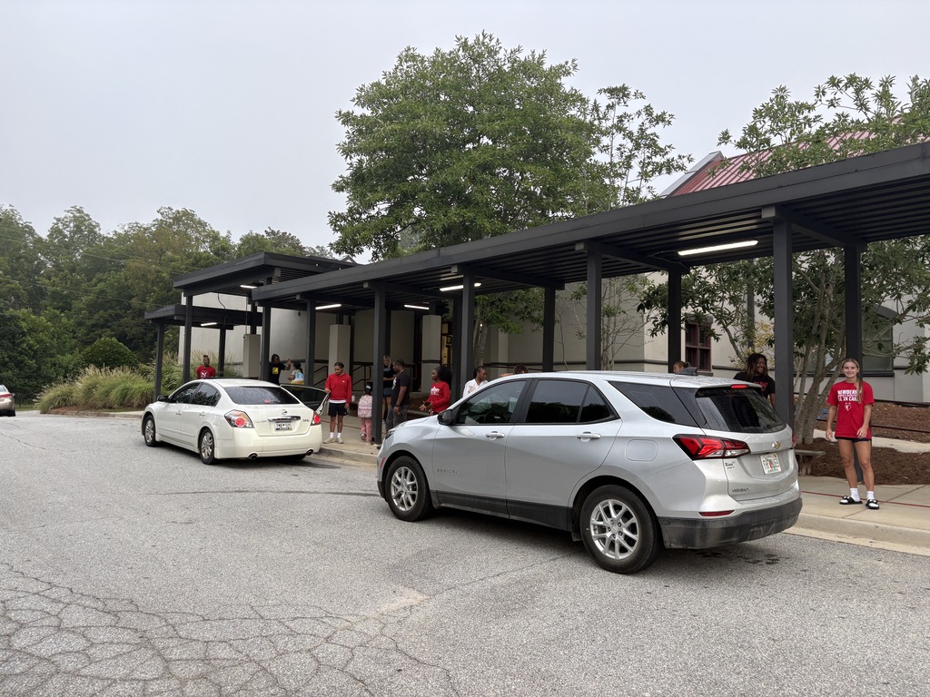 Wide shot of two cars with lots of women opening car doors for our students.