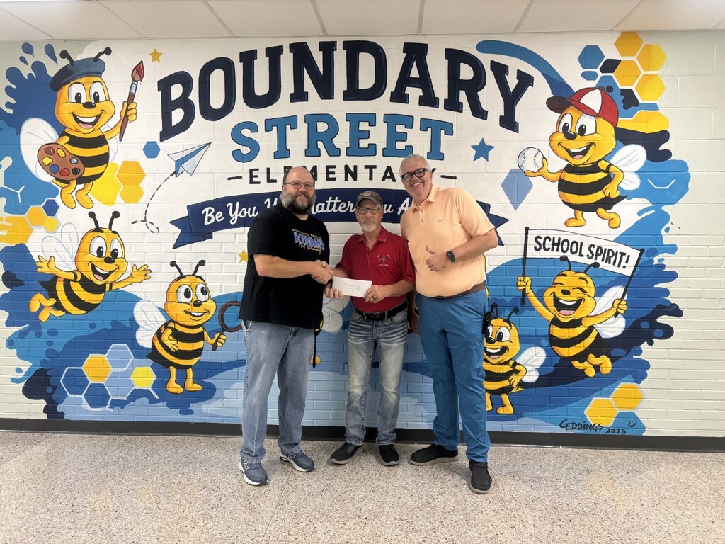 Archery Coach Mikel Eargle (left) shakes hands with Ray Counts of Midstate Quail and Dove (center), who holds a donation envelope. Assistant Principal Mr. Dukes stands beside them in front of Boundary Street Elementary’s bee mural.