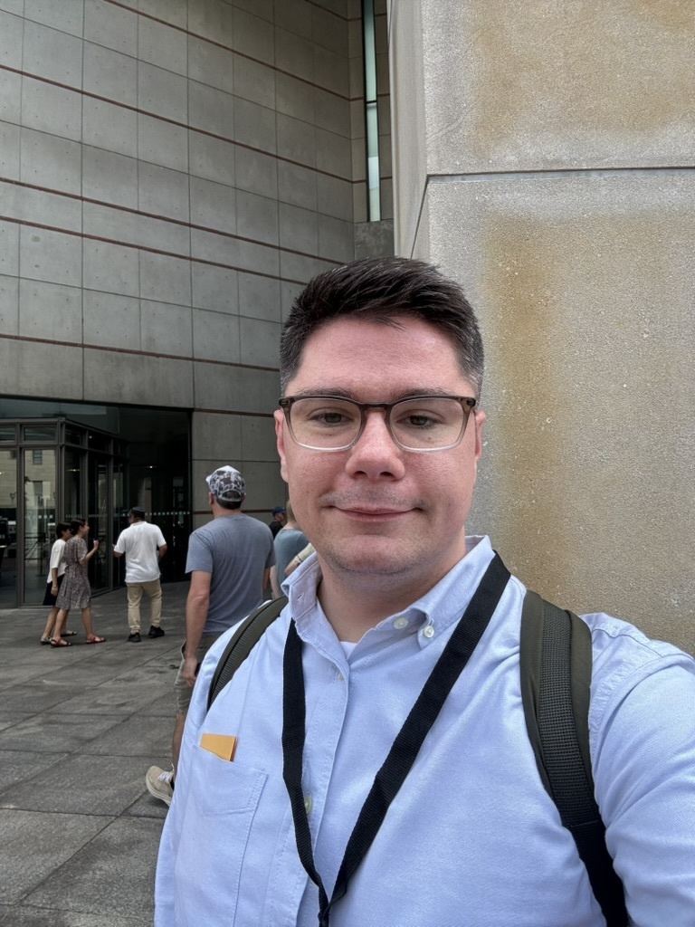 A picture of an adult male standing outside of a building.